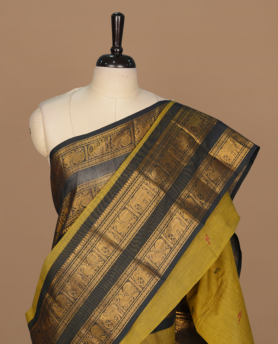 Olive colour chettinad saree featuring gold zari motifs on body, complemented by contrast black colour with traditional border, paired with matching blouse piece.