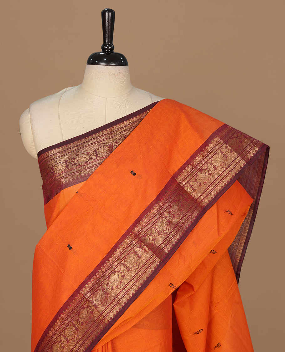 Orange colour chettinad cotton featuring black thread motifs on body, complemented by contrast brown colour with gold zari border, paired with matching blouse piece.