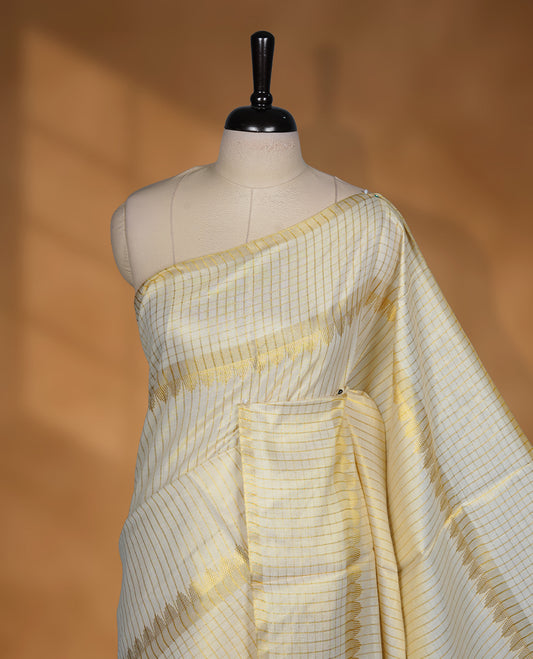 Off white colour Tissue Kerala saree featuring a fine striped and checked body, complemented by a classic golden zari border and traditional pallu design, paired with a matching blouse.