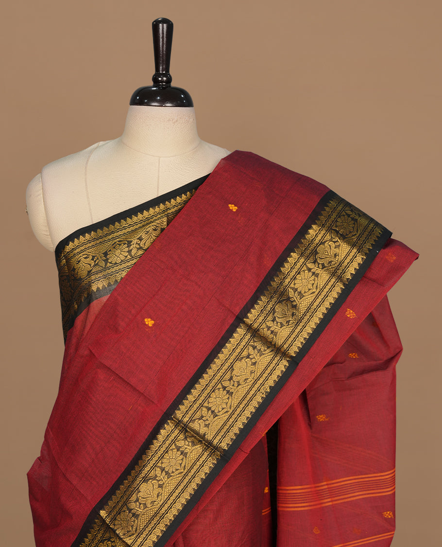 Maroon colour chettinad saree featuring gold zari motifs on body, complemented by contrast black colour with traditional border, paired with matching blouse piece.