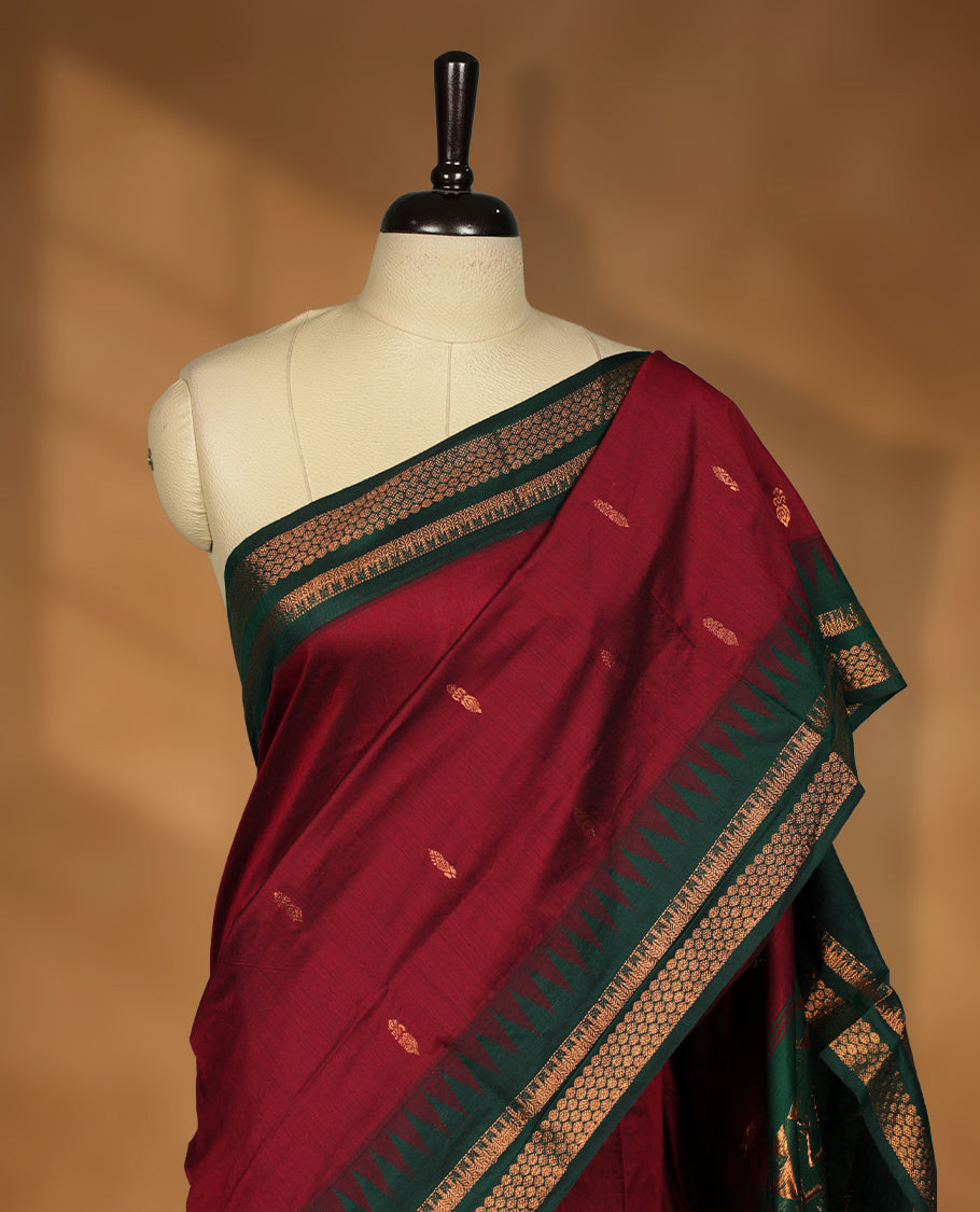 Maroon colour kalyani cotton saree featuring Antique zari motifs on body, contrast green colour border with geometric antique zari pattern, paired with matching blouse piece.