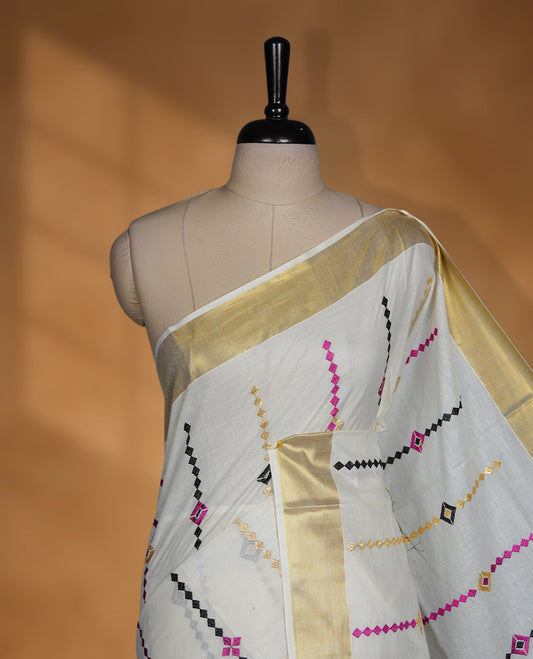 Off white colour cotton Kerala saree featuring colourful geometric motifs, complemented by a classic golden zari border and traditional pallu, paired with a matching blouse.