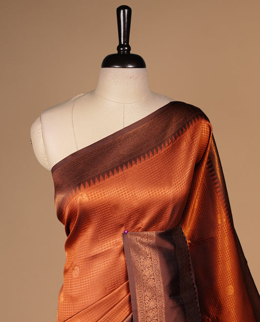 Burnt orange colour silk saree featuring gold zari small square and motifs on body, complemented by contrast chocolate with traditional border, paired with matching blouse piece.