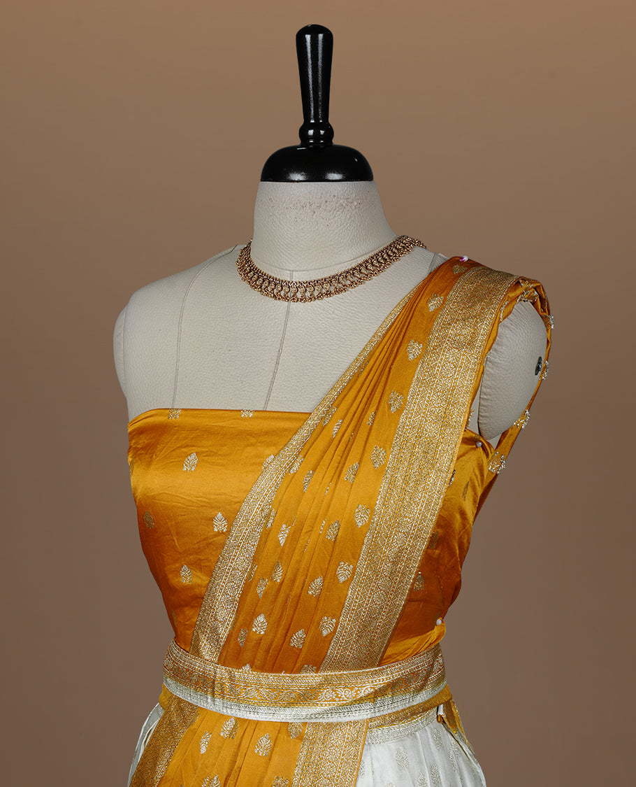 Off white semi banaras semi stitched dhavani set featuring gold zari motifs and contrast Yellow colour and traditional border, unstitched gold zari blouse piece and matching Duptta.