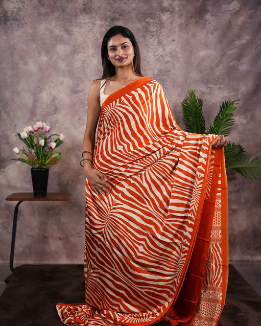 Orange Colour satin model saree featuring Zibra print on body. Ajrak & zibra print on pallu with jhumka tassels, comes with contrast plain blouse piece.