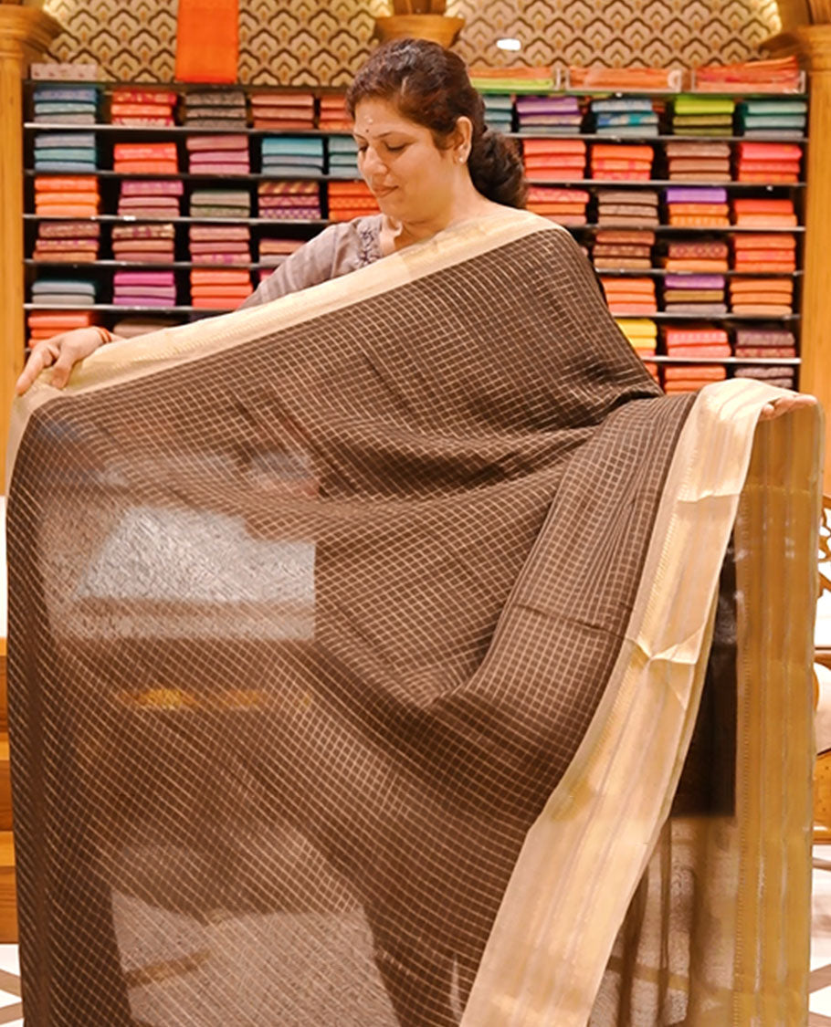 Dark Brown colour moss chiffon saree featuring gold zari checks designed body, complemented by contrast cream colour zari jacquard border, paired with contrast colour blouse piece.