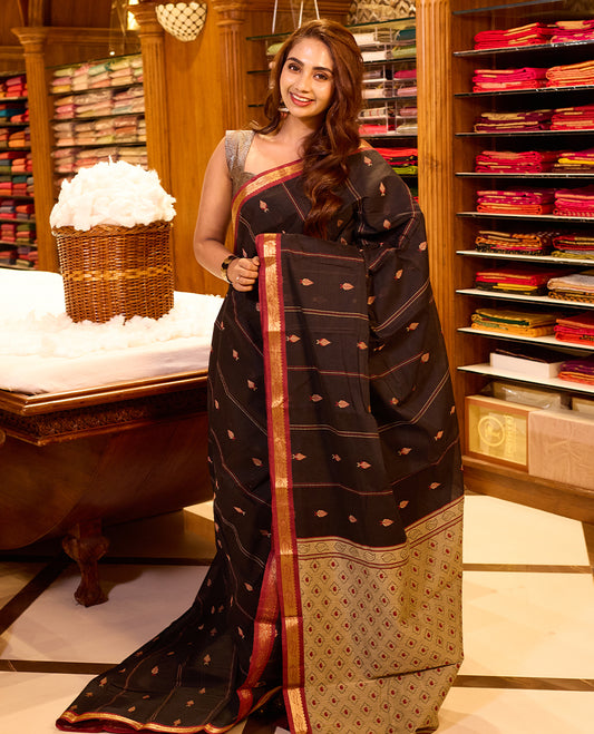 Dark Maroon colour Coimbatore cotton saree featuring subtle woven motifs across the body, paired with a contrast maroon pallu highlighted by a gold zari border, paired with a matching blouse piece.