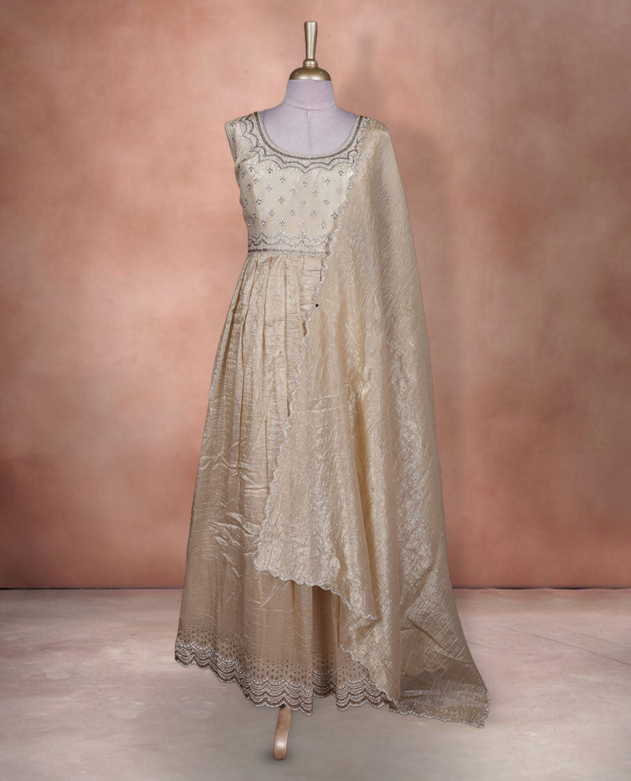 Champagne beige colour stitched gown set with sleeveless embroidered yoke, flared ankle‑length silhouette, and attached dupatta featuring delicate butti work and scalloped beaded edging.