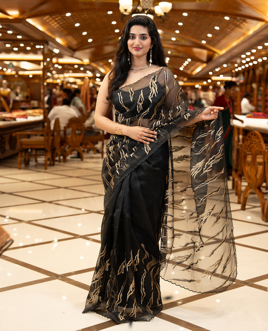 Black colour sheer Organza saree featuring Gold thread embroidery with modern wavy & flame inspired motifs and scallop border, comes with matching organza blouse.