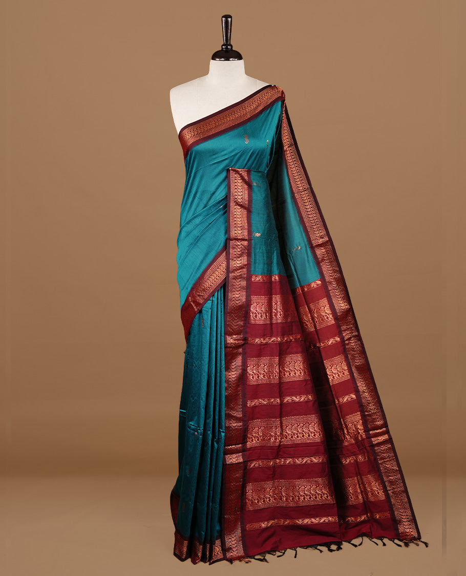Teal green colour kalyani cotton saree featuring gold zari motifs on body, highlighting contrast Maroon colour with Antique gold zari border, paired with matching blouse piece.