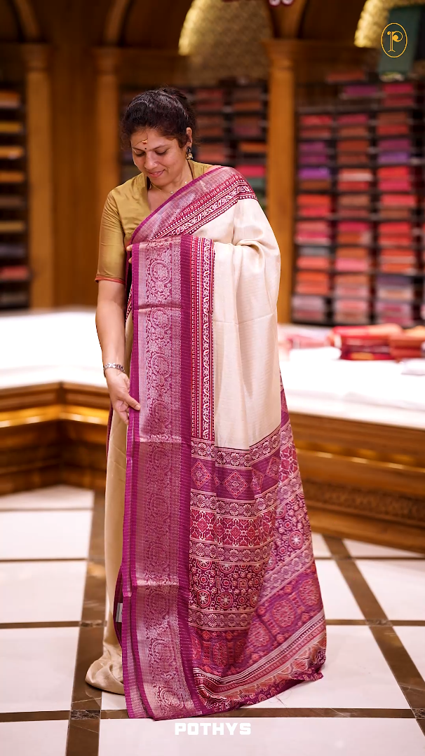 Beige Dolla silk saree featuring antique zari stripes across the body, adorned with a striking Ajrak and Traditional Purple colour border, ajrak printed pallu and paired with a perfectly matching blouse.