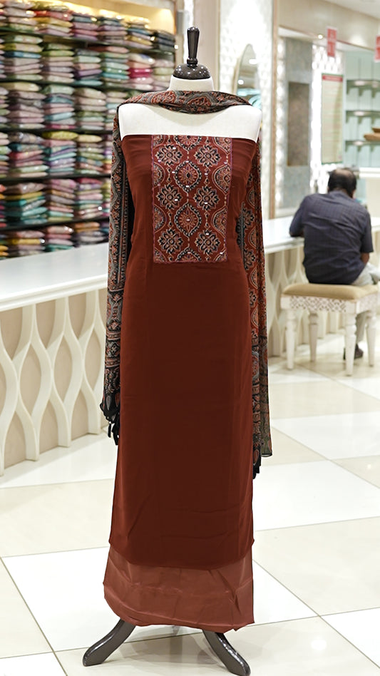 Brick red Georgette salwar material featuring Ajrakh print with mirror work on the yoke, paired with Ajrakh printed dupatta with mirror detailing and plain bottom.