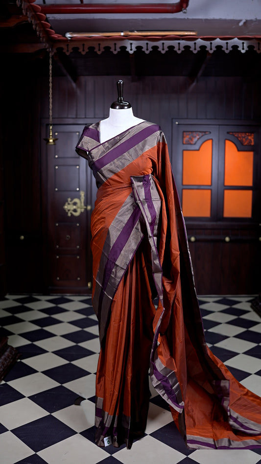 Burnt Orange colour Arani Silk saree featuring a plain body with elegant contrast Purple borders, comes with a matching blouse piece.