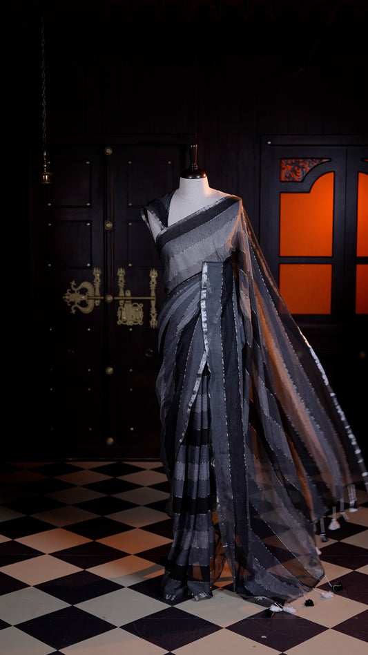 Black colour Mul Mul cotton saree adorned with subtle silver stripes across the body and finished with a delicate silver zari border.