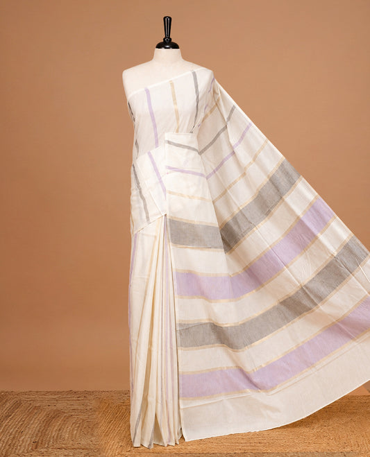 Off White Colour Cotton Kerala Saree Featuring Light Gold, Grey And Purple Zari Stripes On The Body, Enhanced By A Traditional Zari Border And Pallu, Paired With A Matching Blouse Piece.