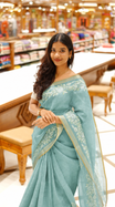 Teal mist colour linen tissue saree featuring Floral design with Aari work & contrast simple border, comes with matching blouse piece.