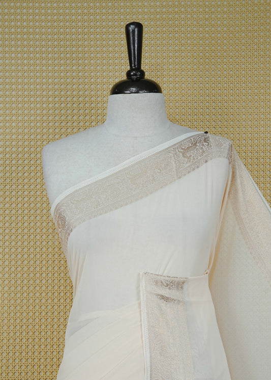 Cream colour georgette saree having plain body, peacock & deer gold zari detailed border, comes with matching blouse piece