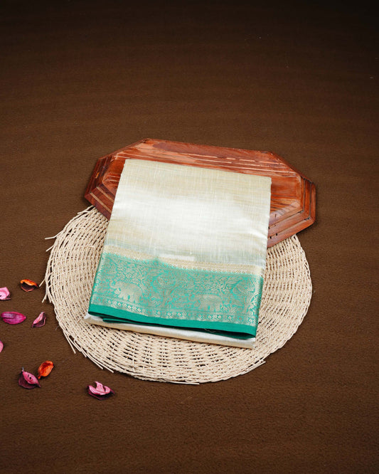 Cream colour Tussar silk saree Featuring Plain body, complemented by Contrast green colour gold zari elephant & tree motifs on border, paired with matching blouse piece.
