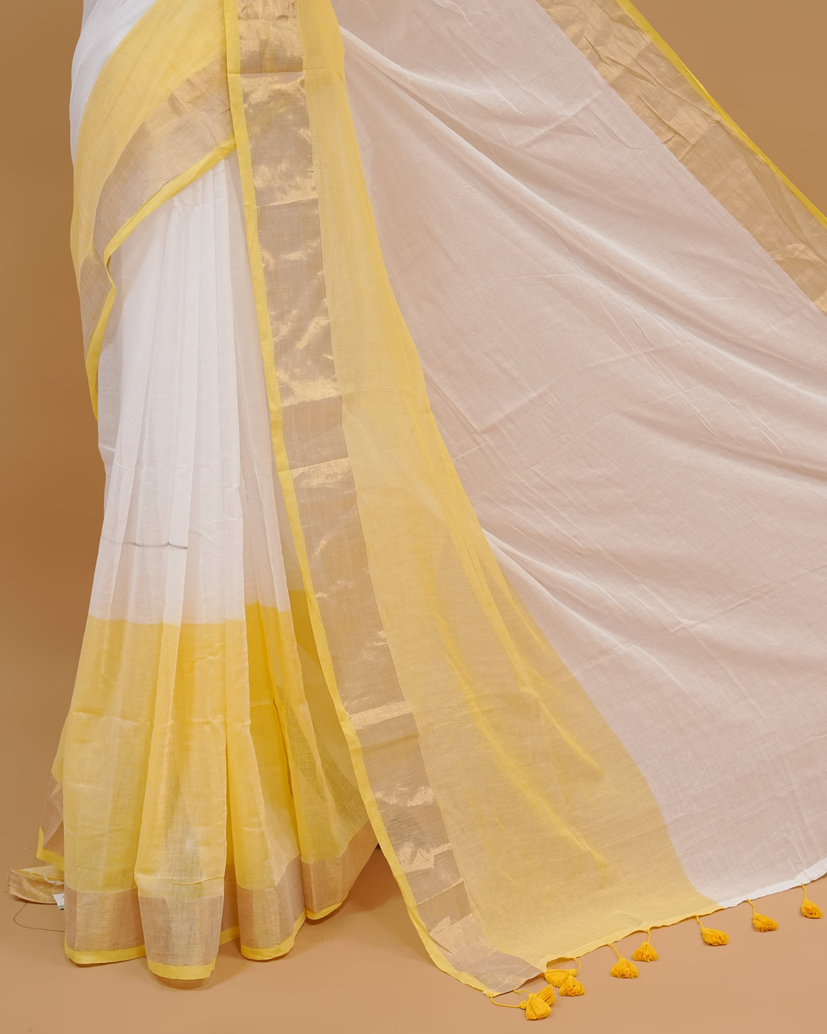 White colour Mul cotton saree featuring Elegant Plain body, complemented by contrast yellow & gold zari border & Tassels.