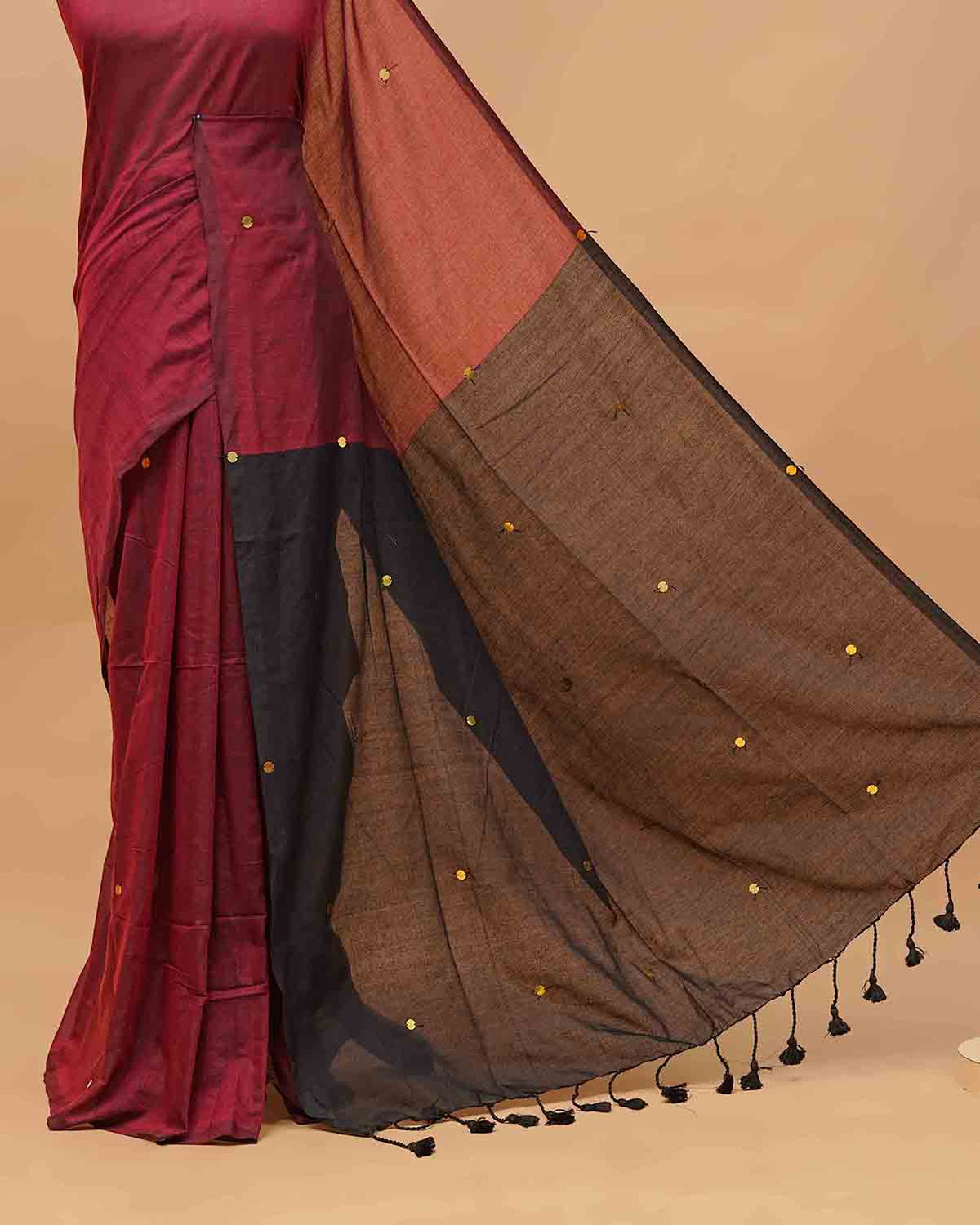 Black and Maroon coloured half and half mul cotton saree featuring elegant sequin detailing on the body, finished with a beautiful pallu adorned with tassels.