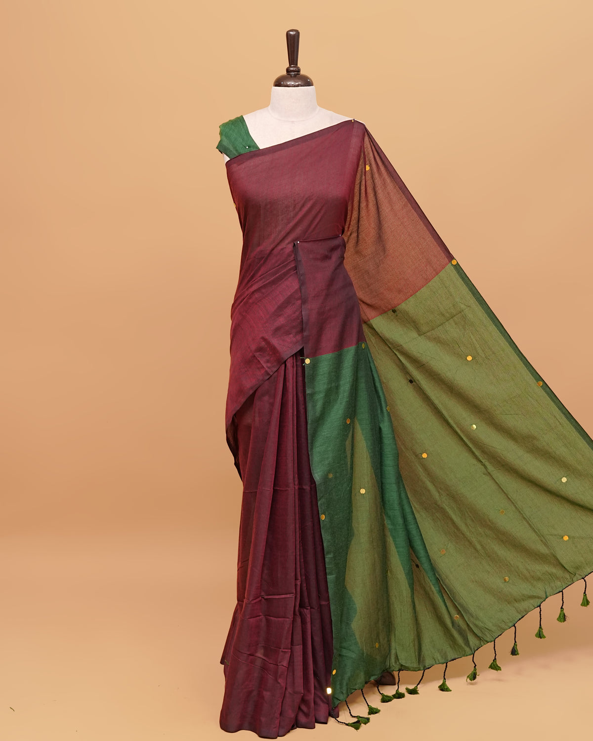 Maroon and Green coloured half and half mul cotton saree featuring elegant sequin detailing on the body, finished with a beautiful pallu adorned with tassels.