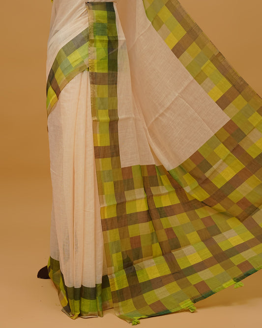 Cream colour semi linen saree featuring a plain body, a multicoloured check design with a gold tissue border, and a pallu finished with Tassels. Paired with a matching blouse piece.