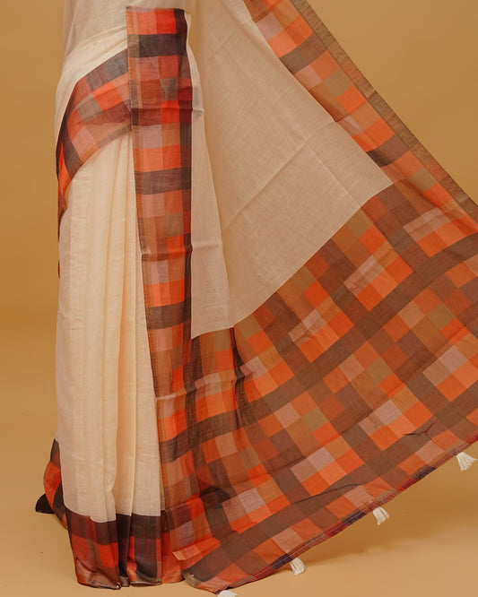 Cream colour Semi linen saree featuring Plain body, a multicoloured check design with a gold tissue border,, and a pallu finished with White tassels, Paired with a matching blouse piece.