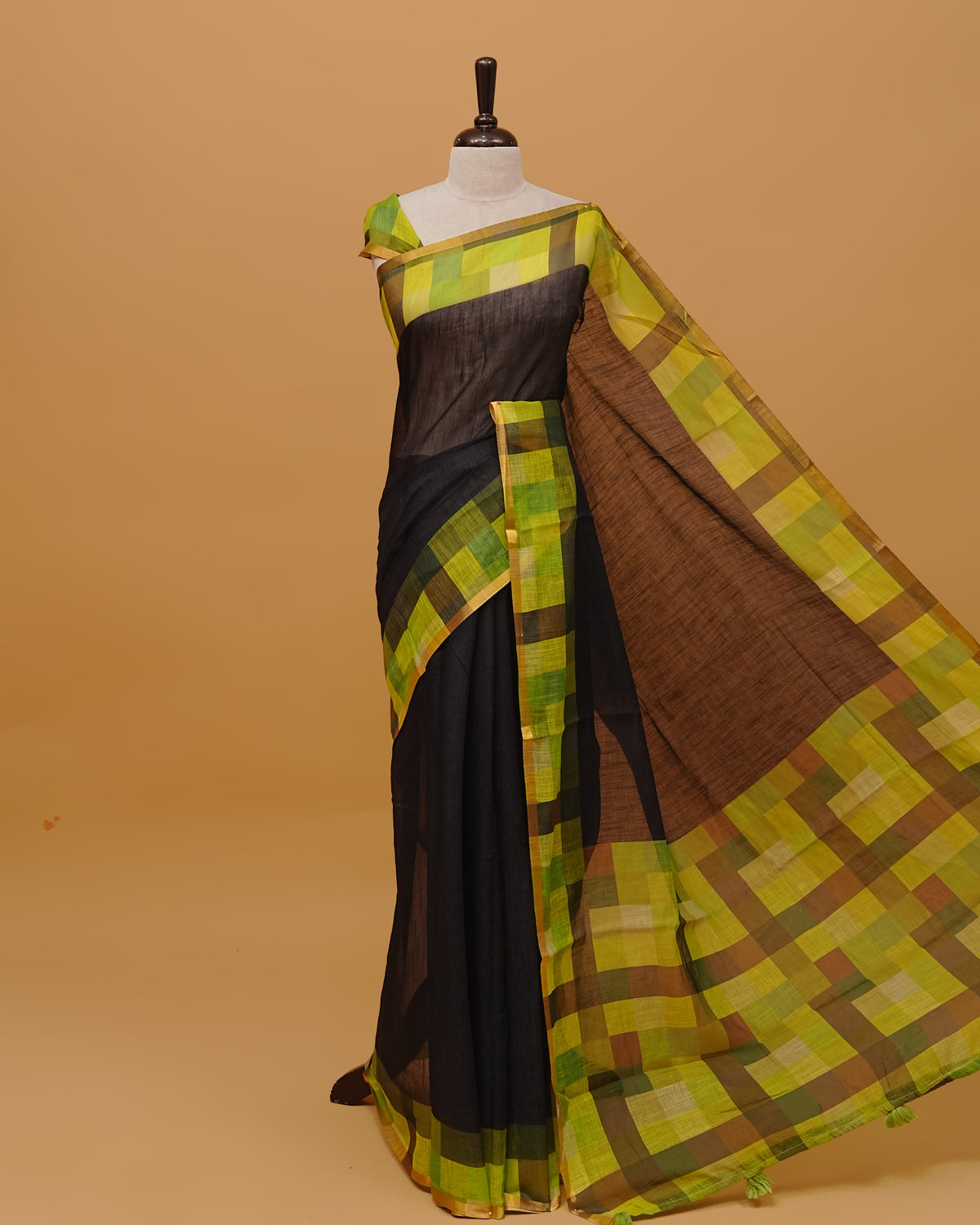 Black colour Semi linen saree featuring a plain body, Multi coloured check design with a Gold tissue simple border, and a pallu finished with Green tassels, Paired with a matching blouse piece.