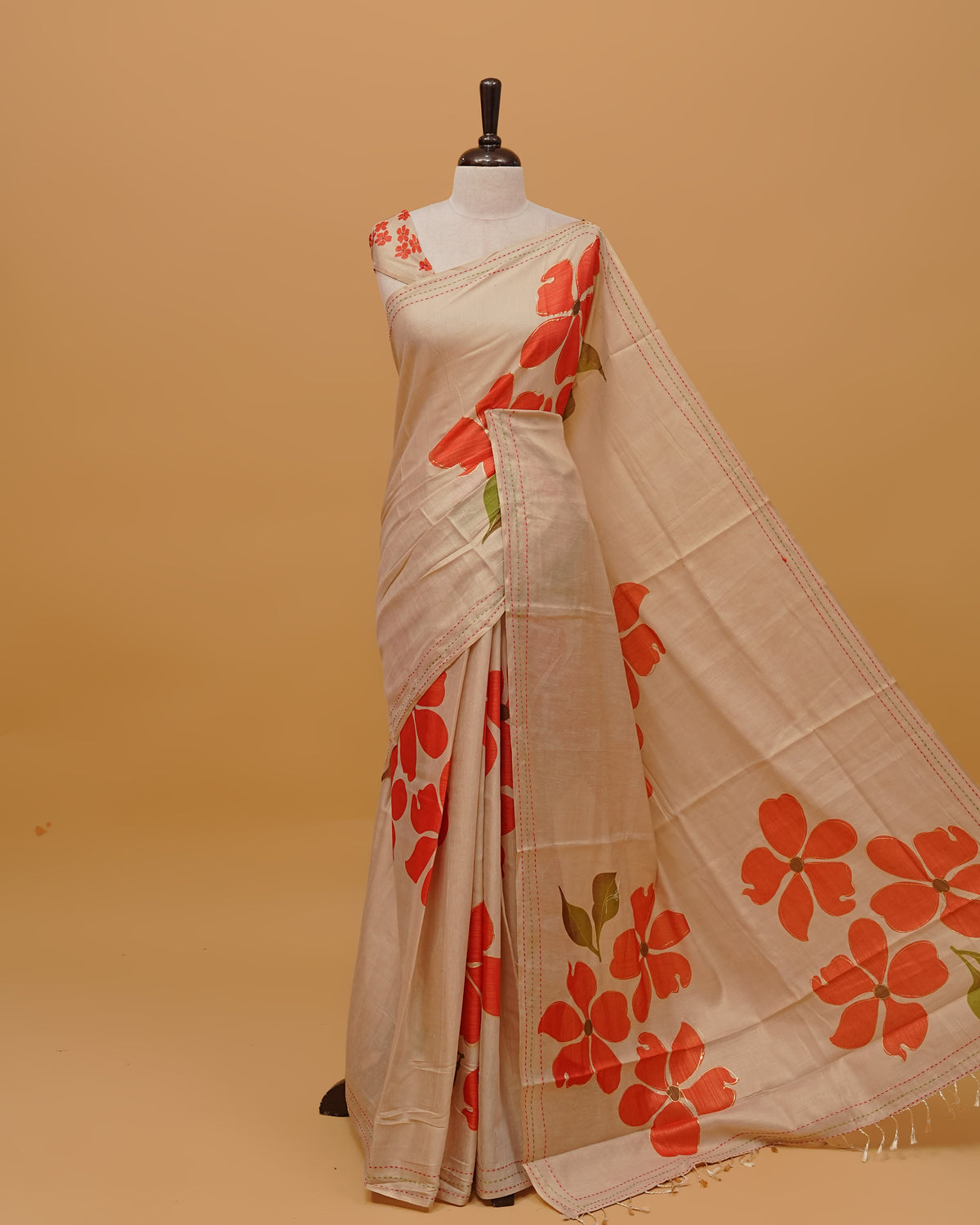 Cream colour Semi Tissue saree featuring Red colour Floral Motifs on body, a Threaded border & pallu,finished with tassels, paired with a matching blouse piece.