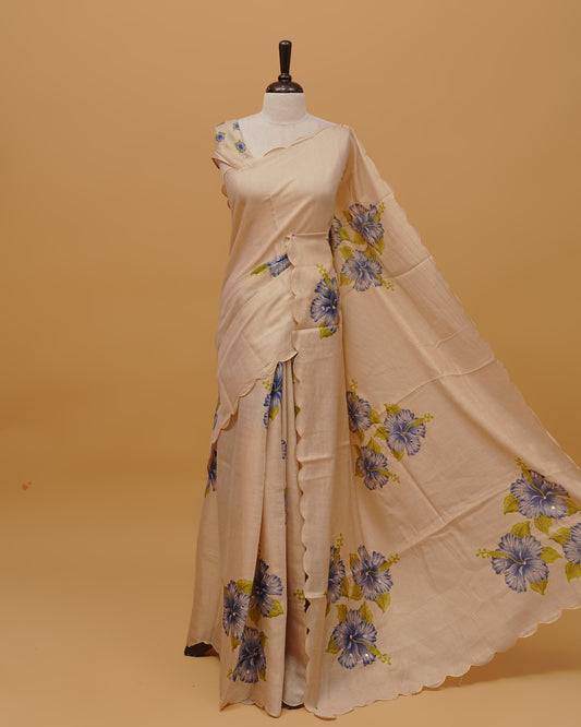 Cream colour Semi Tissue saree featuring Floral Motifs on body, a Gold Simple scalloped border, a pallu finished with tassels, paired with a matching blouse piece.