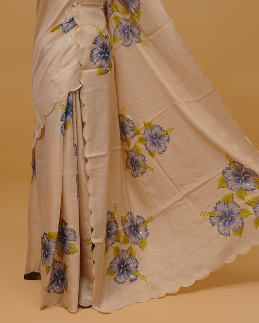 Cream colour Semi Tissue saree featuring Floral Motifs on body, a Gold Simple scalloped border, a pallu finished with tassels, paired with a matching blouse piece.