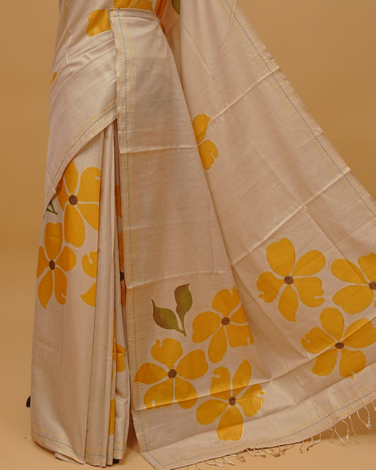 Cream colour Semi Tissue saree featuring  Yellow colour Floral Motifs on body, a Threaded border, a pallu finished with tassels, paired with a matching blouse piece.