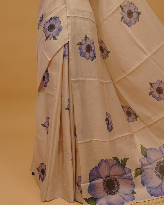 Cream colour Semi Tissue saree featuring Light Purple Floral Motifs on body, a Gold Simple Border & pallu finished with tassels, paired with a matching blouse piece.