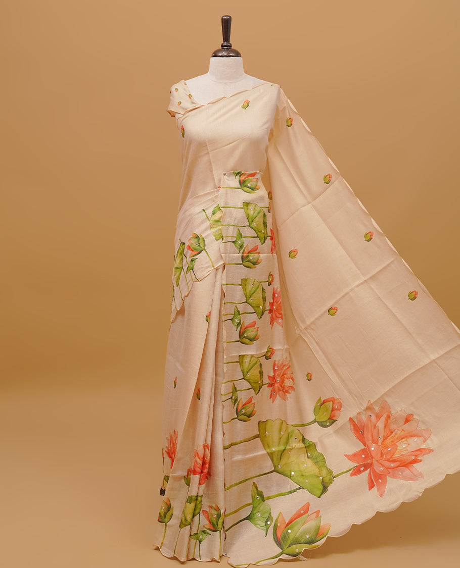 Cream colour semi tissue saree featuring Floral prints with Mirror Work on the body, with scallop border & pallu finished with tassels. Paired with a matching blouse piece.