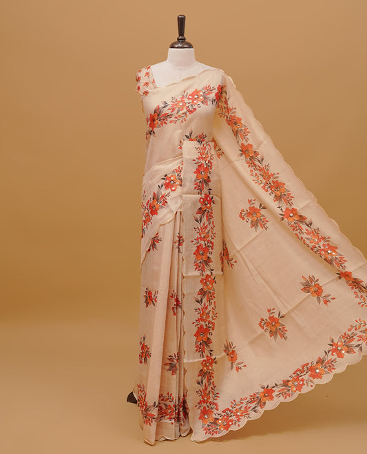 Cream colour semi tissue saree featuring floral prints with Mirror Work on body, with scallop border & pallu finished with tassels. Paired with a matching blouse piece.
