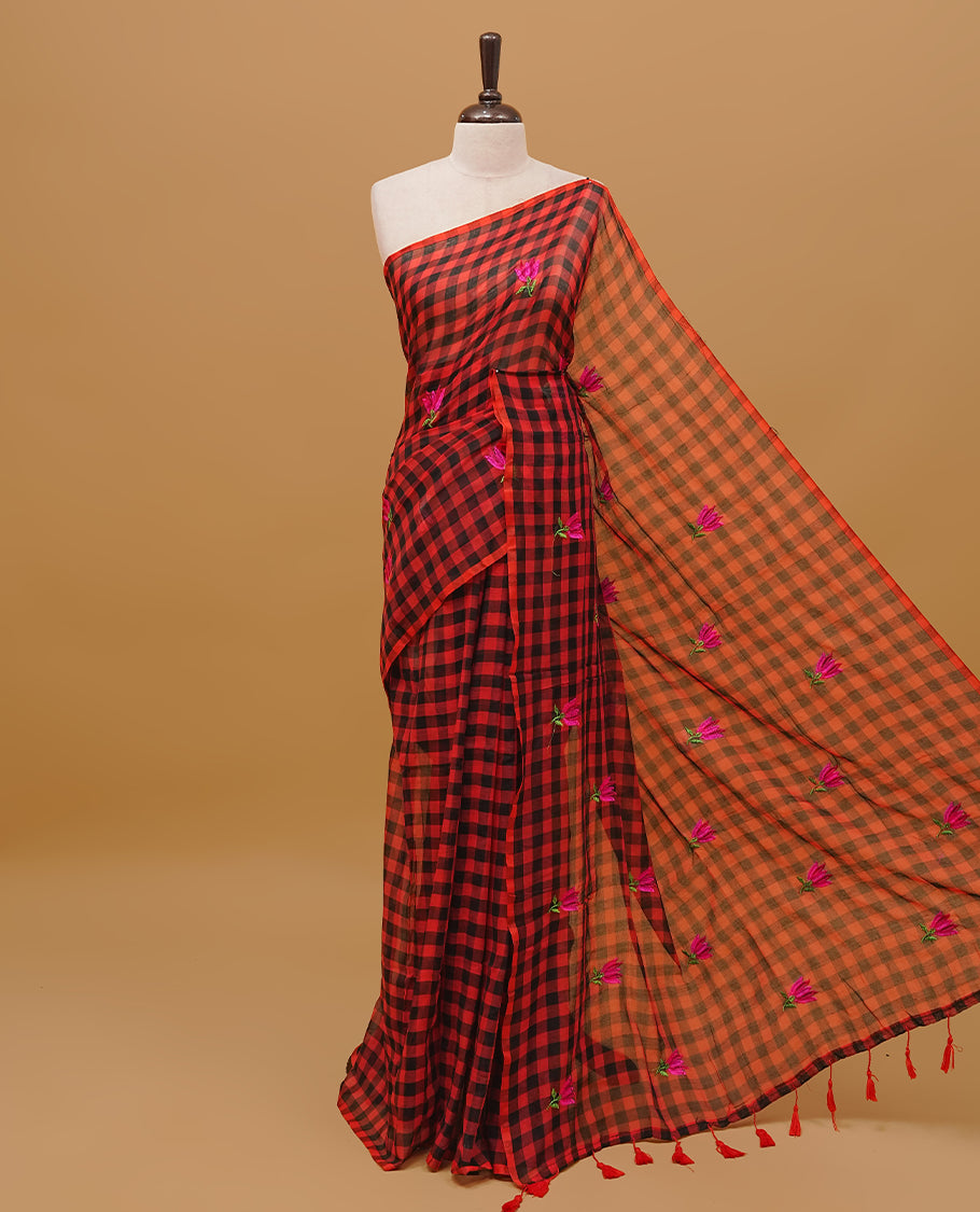 Red and black colour mul cotton saree featuring floral thread work in checked body & pallu finished with tassels. Paired with a matching blouse piece.