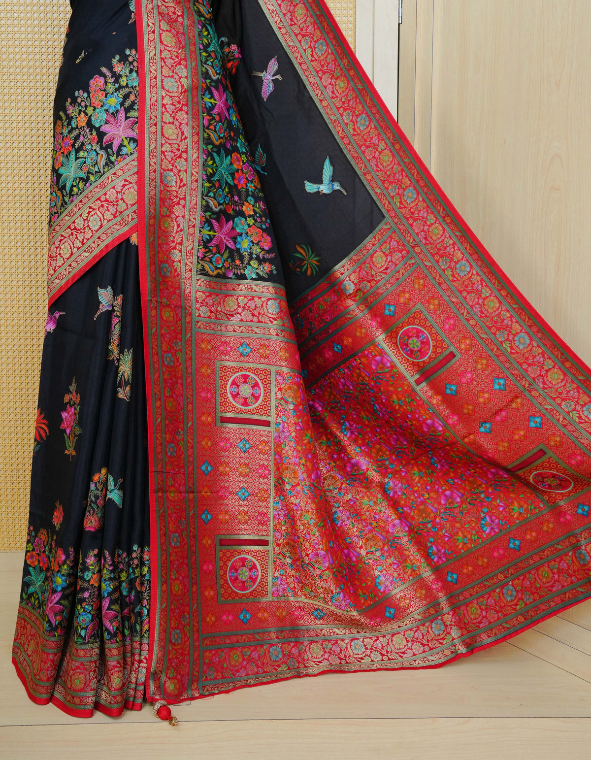 Black Colour Pashmina Saree featuring multi colour flower patterns on body, complemented by Contrast red colour floral motifs zari patterns on border and Pallu, comes with matching blouse piece