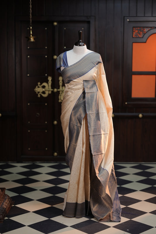 Cream colour semi tissue saree highlighting golden thread worked body, contrast blue colour border, pallu and comes with matching blouse piece.