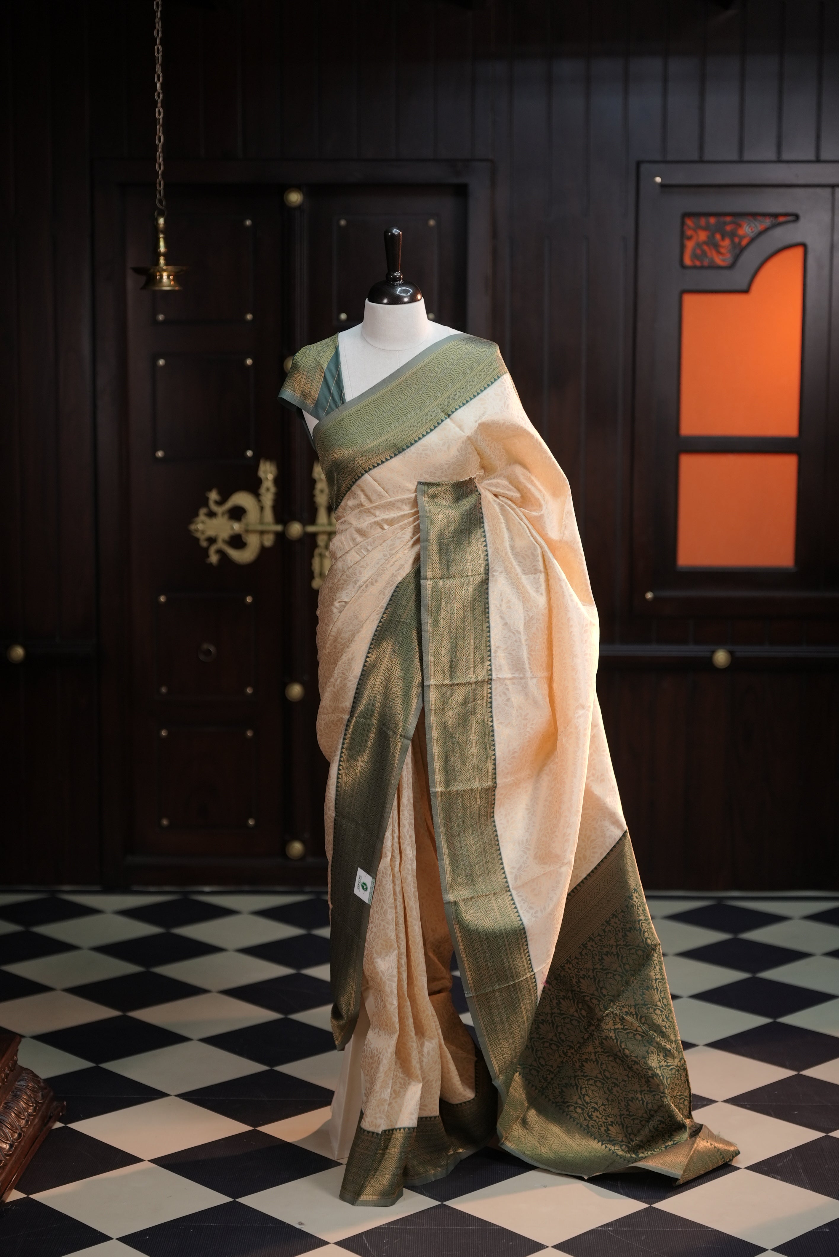 Cream colour semi tissue saree highlighting golden thread worked body, contrast green colour border, pallu and comes with matching blouse piece.