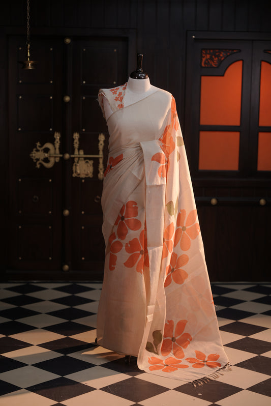 Beige colour semi soft tissue saree adorned with bold Orange floral prints across the body, designed without a border, paired with a matching blouse piece featuring delicate flower motifs.