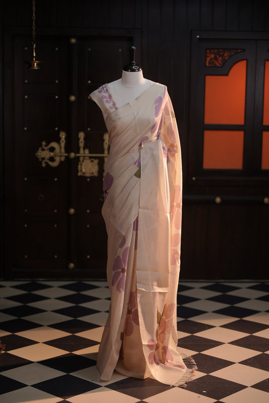 Beige colour semi soft tissue saree adorned with bold Lavender floral prints across the body, designed without a border, paired with a matching blouse piece featuring delicate flower motifs.