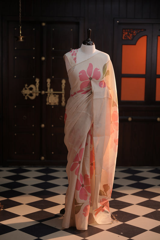 Beige colour semi soft tissue saree adorned with bold Pink floral prints across the body, designed without a border, paired with a matching blouse piece featuring delicate flower motifs.