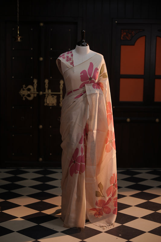 Beige colour semi soft tissue saree adorned with bold magenta floral prints across the body, designed without a border, paired with a matching blouse piece featuring delicate flower motifs.
