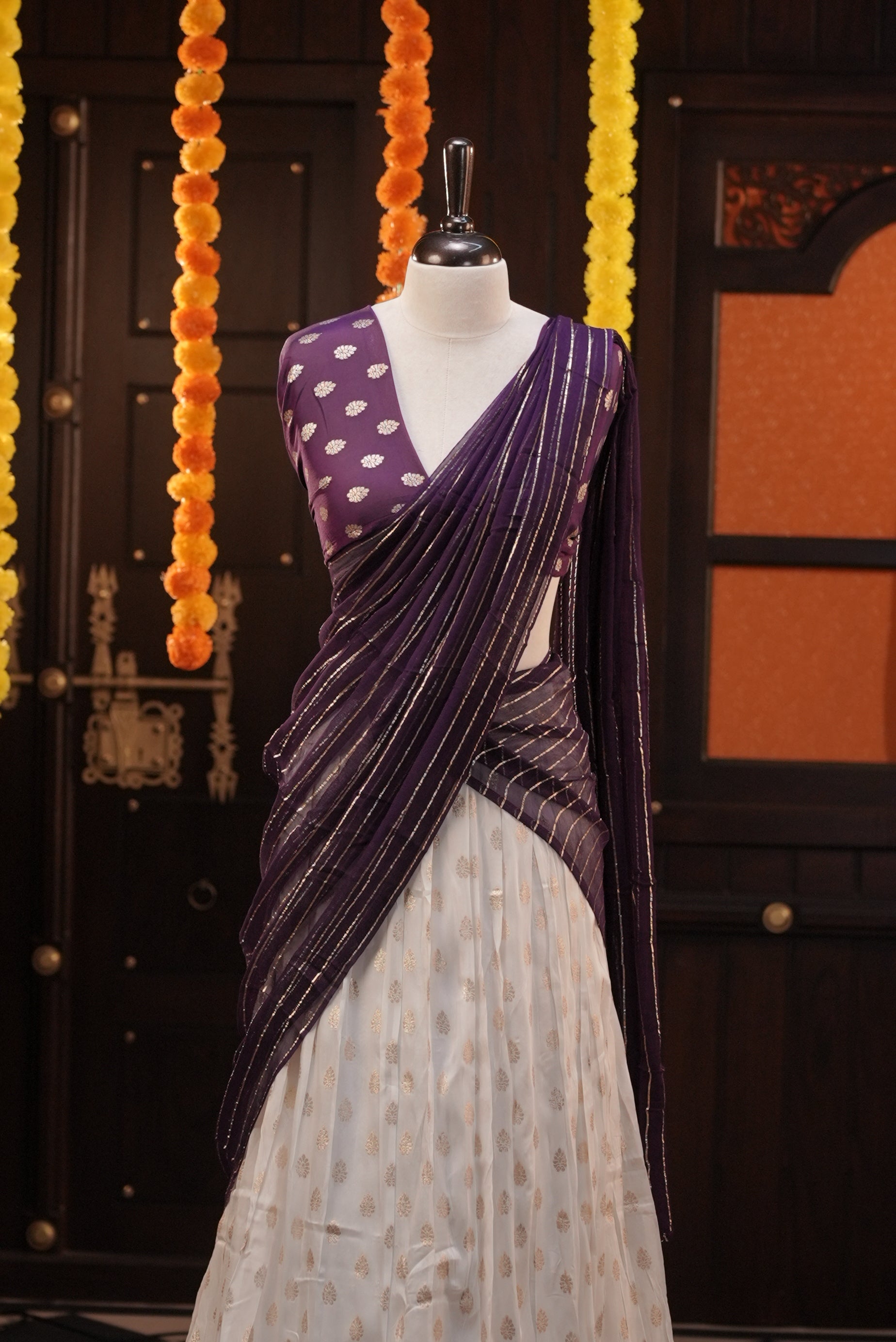Off white colour Semi Stitched Banaras Dhavani Set Featuring off white Skirt with Gold zari buttas & Traditional border, paired with Purple colour Blouse material with gold zari buttas, finishing with same colour with gold zari Stripped Dupatta.