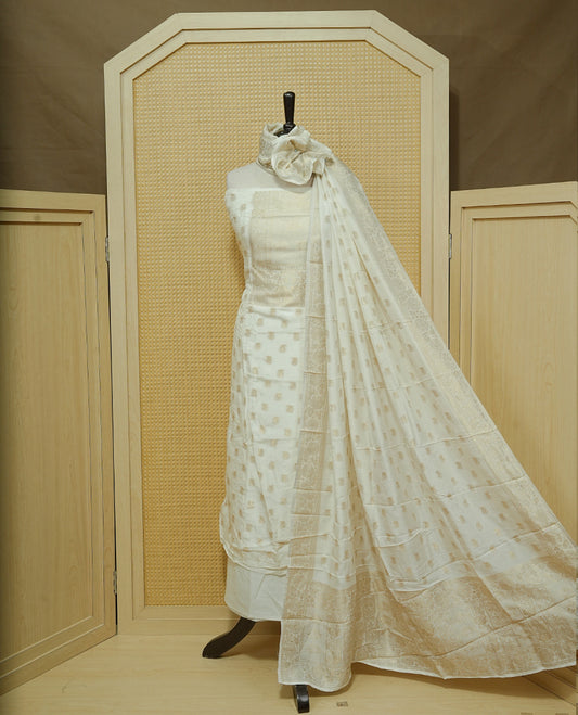Cream colour Salwar material featuring gold zari Buttas on body & zari worked Neck Portion, paired with matching dupatta & Bottom.