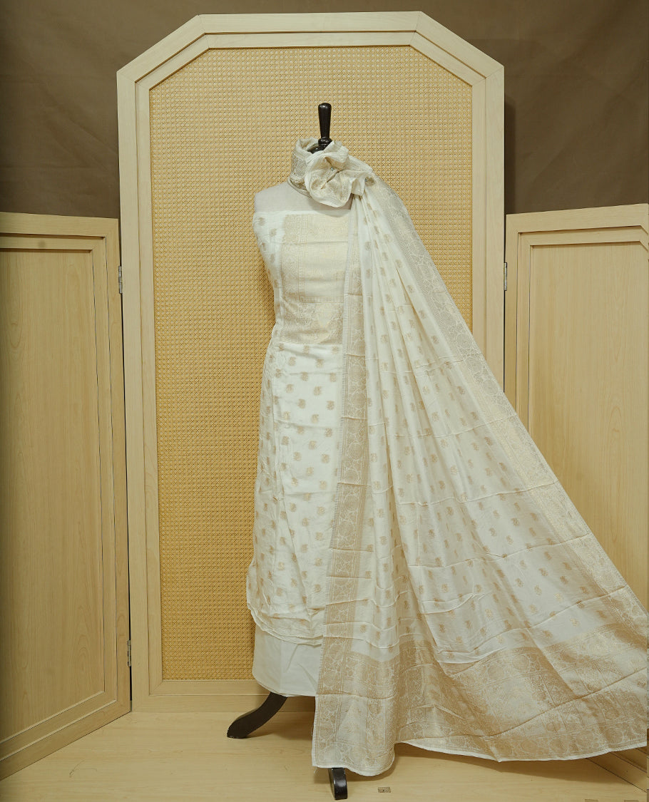 Cream colour Salwar material featuring gold zari Buttas on body & zari worked Neck Portion, paired with matching dupatta & Bottom.