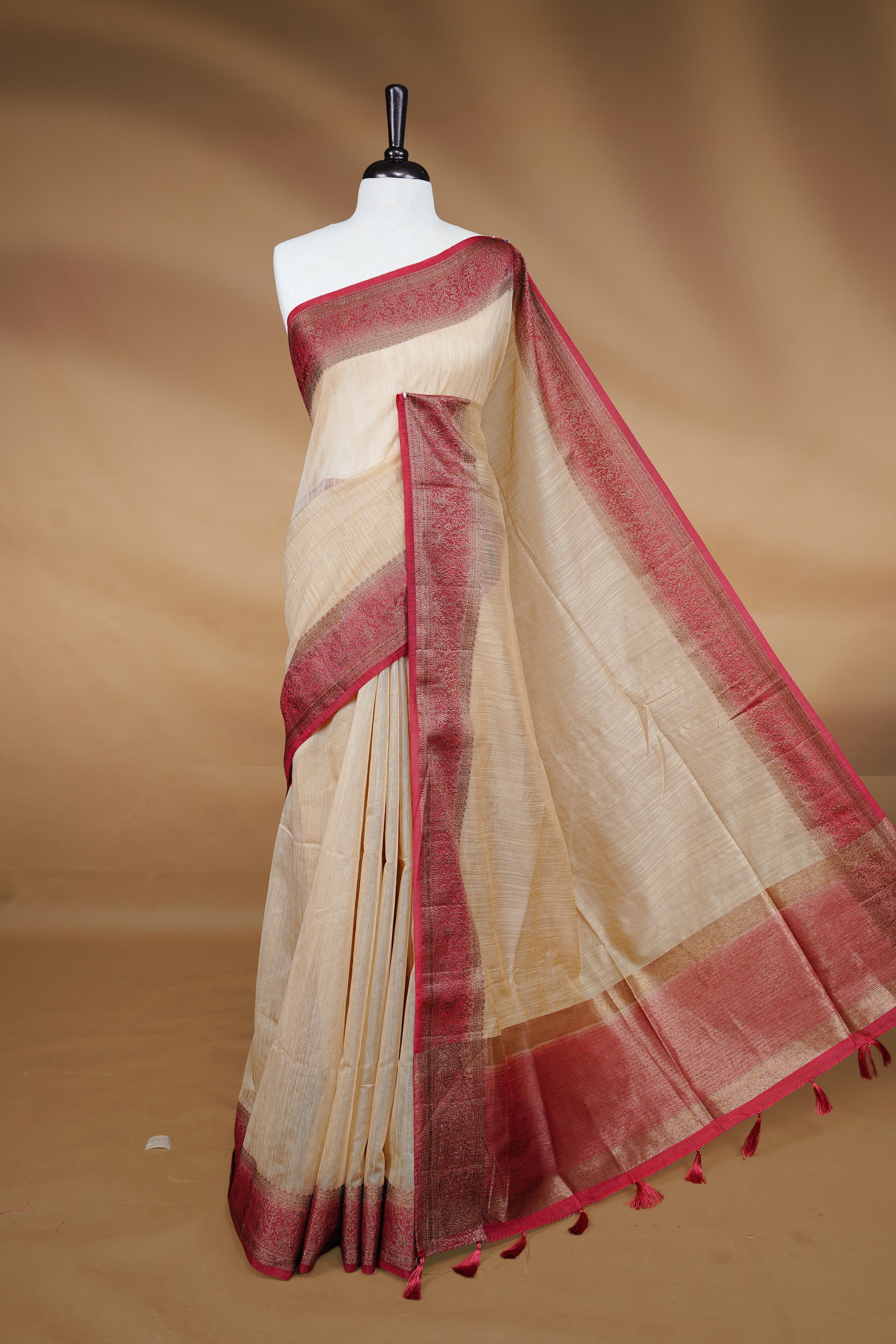 Biege colour Semi linen saree featuring Elegant plain body, complemented by contrast Maroon colour With Antique zari border, paired with matching blouse piece.