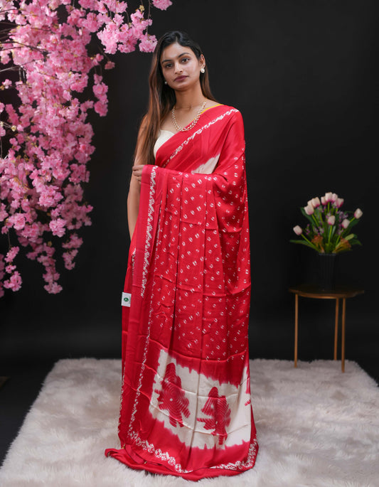 Deep Red coloured modal satin saree featuring a plain cream coloured body, complemented by a double shaded border and a Bandhani designed pallu with jhumka tassels. Paired with a matching contrast coloured blouse piece.