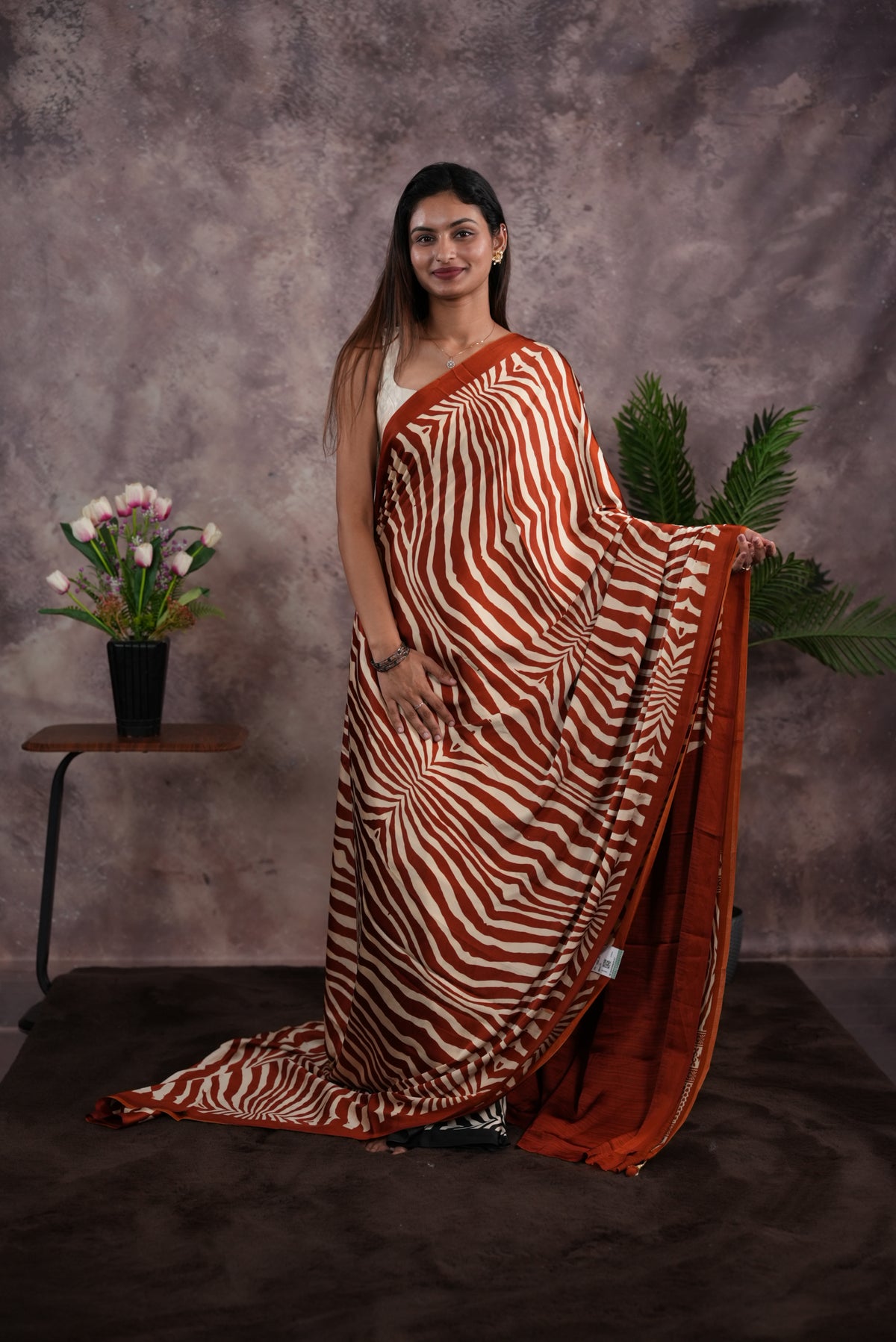 Rust Orange Colour satin model saree featuring Zibra print on body. Ajrak & zibra print on pallu with jhumka tassels, comes with contrast plain blouse piece.