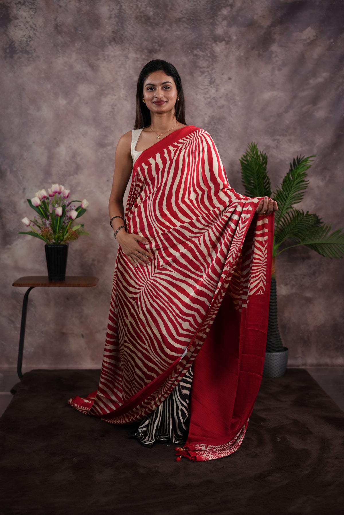 Red Colour satin model saree featuring Zibra print on body. Ajrak & zibra print on pallu with jhumka tassels, comes with contrast plain blouse piece.